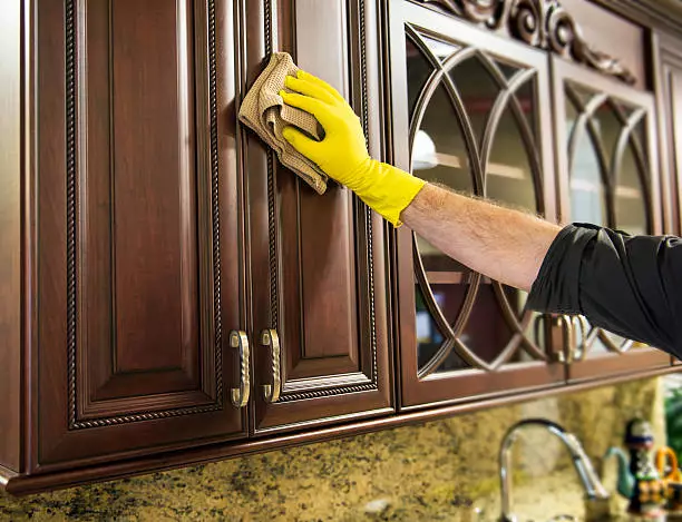 man cleaning a wooden kitchen cabinet.